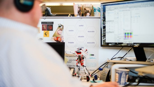 A photo over a designer's shoulder of his workstation and computer screen